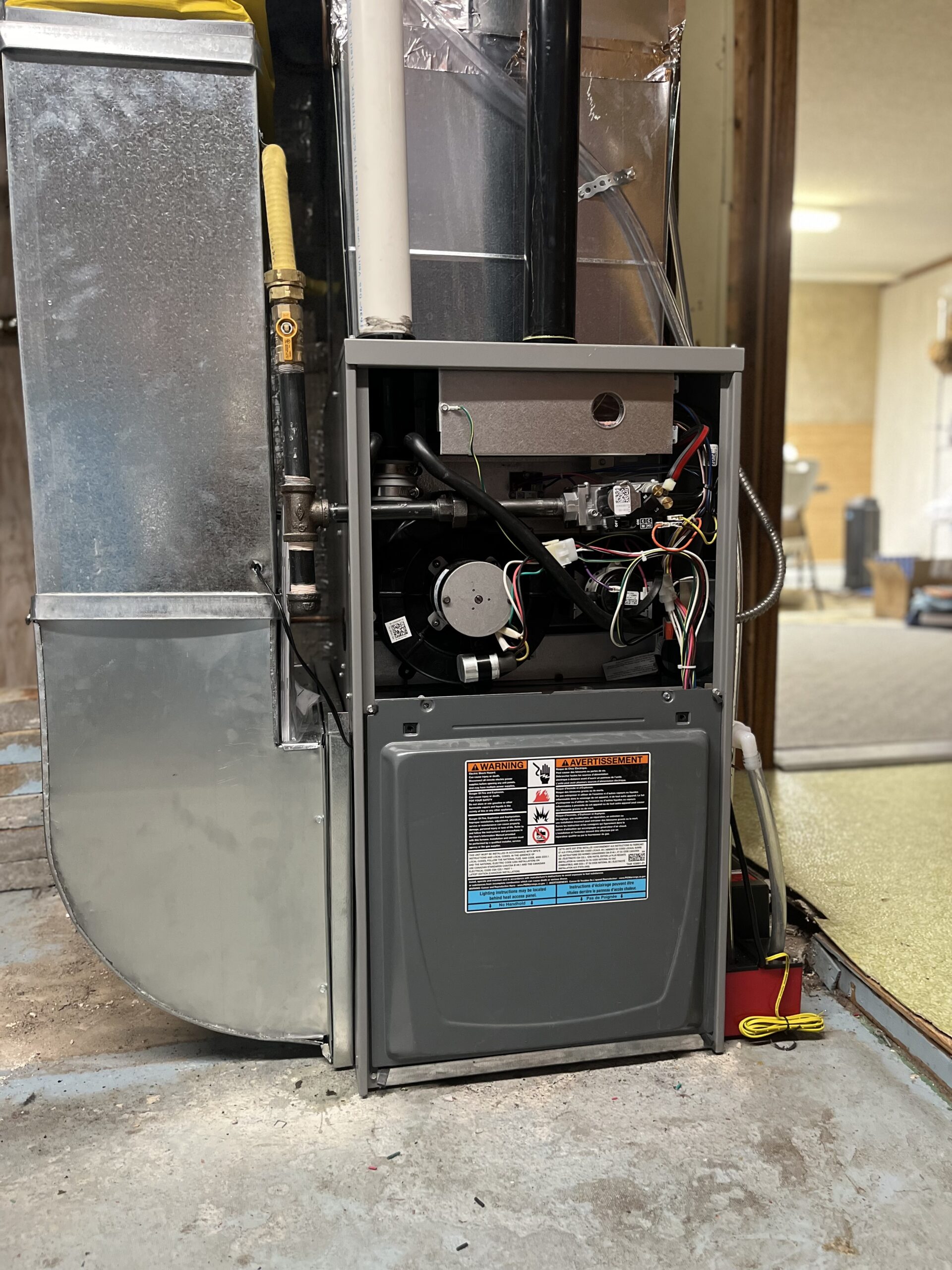 IMG_0241 A modern furnace with its front panel open, exposing internal components and wiring, stands on a basement floor next to ductwork and a yellow gas line—expertly serviced by Family Plumbing and Heating.