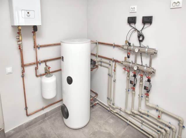 A modern boiler room with a hot water tank, various pipes, valves, meters, and wall-mounted electrical outlets—expertly maintained by Regina plumbing services.